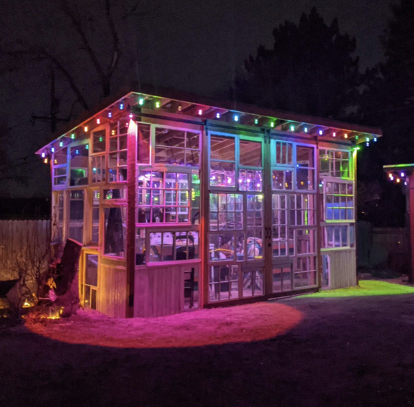A colorful greenhouse decorated with rainbow fairy lights at night.